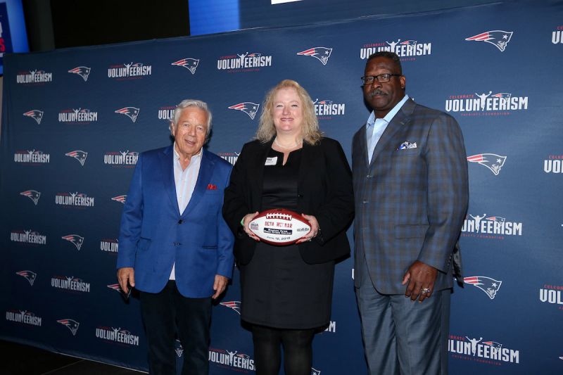 Robert Kraft, Beth Molnar holding football, and Andre Tippett, in front of Patriots backdrop.