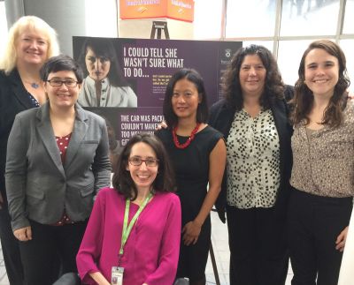 Group of six BARCC staff and board members in front of car card with MBTA campaign to end sexual harassment on the T