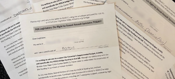 A set of letters urging Boston legislators to support funding for rape crisis centers and services for sexual assault survivors is spread out on a dark surface.