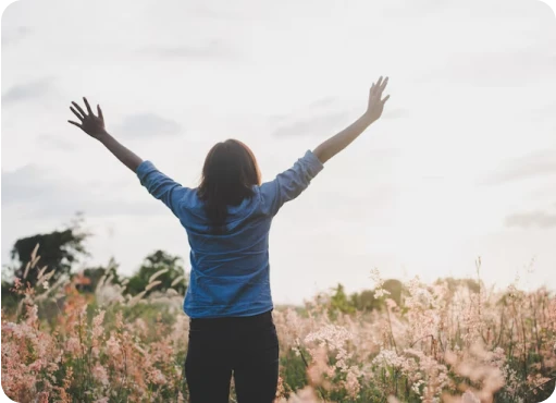 BARCC Resources Image 03 Person standing in a field with arms raised, facing the sky during daylight.