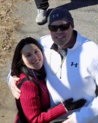 Sonia_and_Jon_1 A man and a woman embrace outdoors in cold weather attire, wearing sunglasses and smiling.
