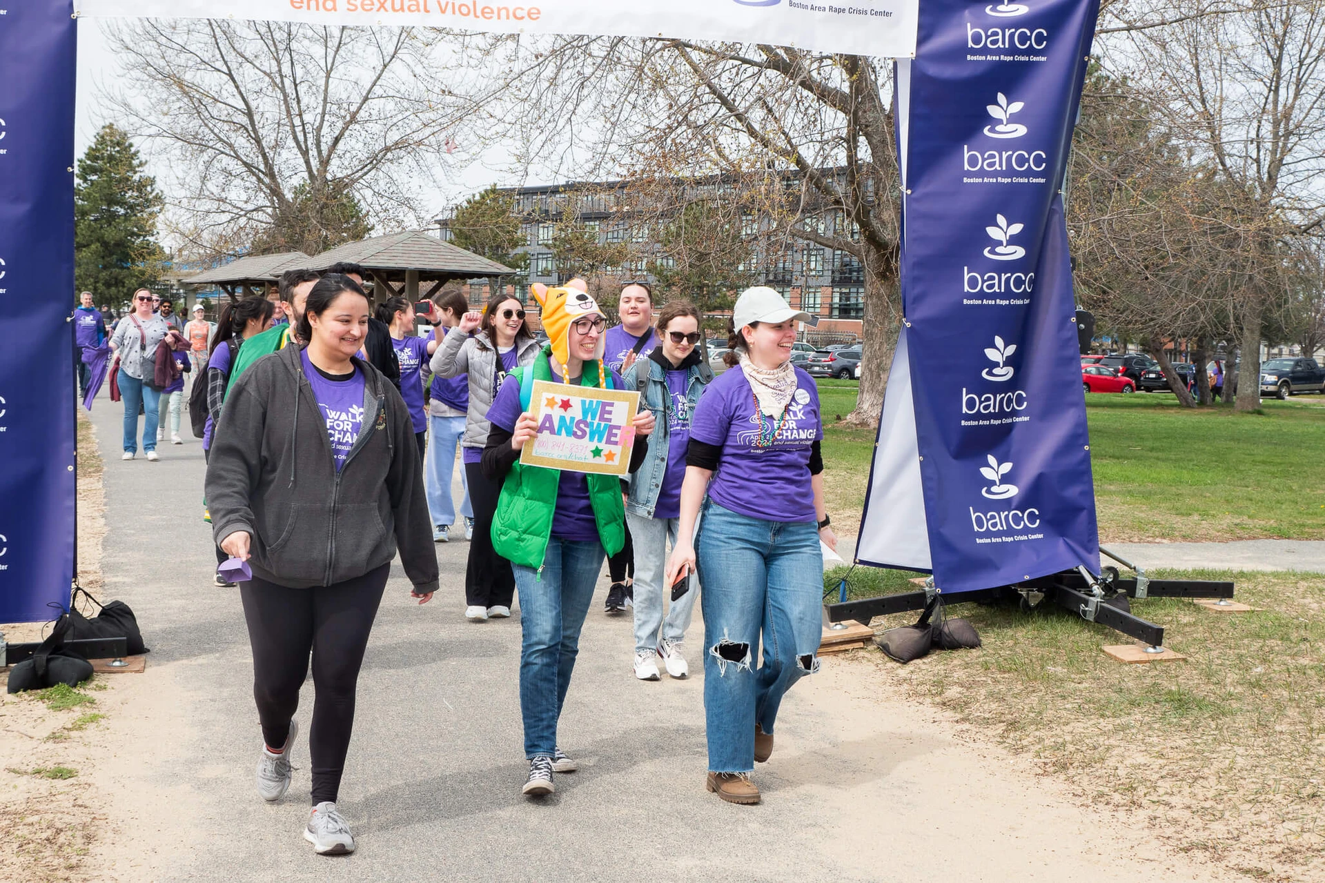 20240420-553 A group of people walk under a banner at an outdoor event focused on the education and prevention of sexual violence, with one person proudly holding a sign that says "We Can Soar.