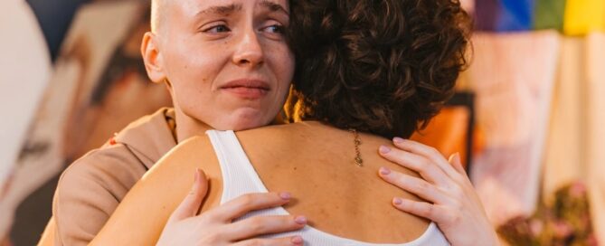 Two people embracing, one with a shaved head appearing emotional, in a vibrantly decorated room. It's a touching scene reminiscent of the supportive services you might find in Boston where people get help when they need it most.