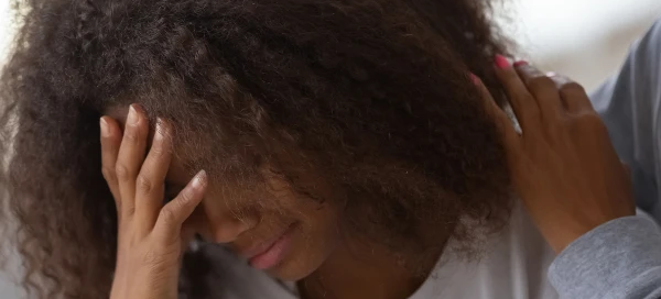 A person with curly hair holds their head in one hand, appearing distressed, while another provides comfort with a hand on their shoulder. This empathetic gesture embodies the supportive environment of a Boston rape crisis center, where compassionate services can make all the difference.