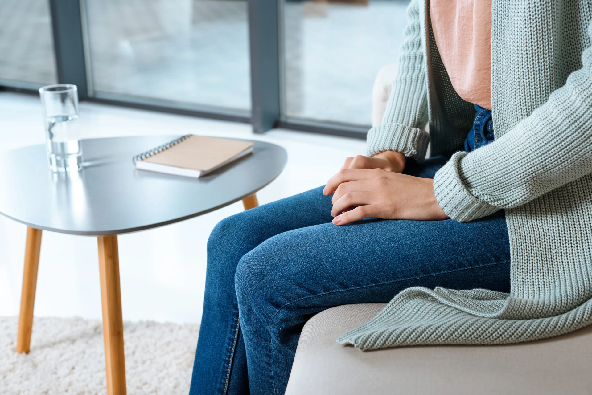 A person sits on a couch in Boston, MA, hands clasped on their lap, near a small table with a notebook and a glass of water, contemplating prevention strategies.