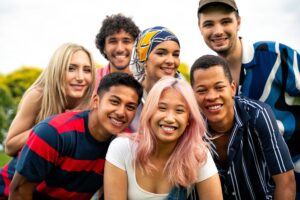 Un grupo de siete personas sonriendo al aire libre, con una mezcla de estilos de ropa y peinados, posando de cerca para una fotografía.
