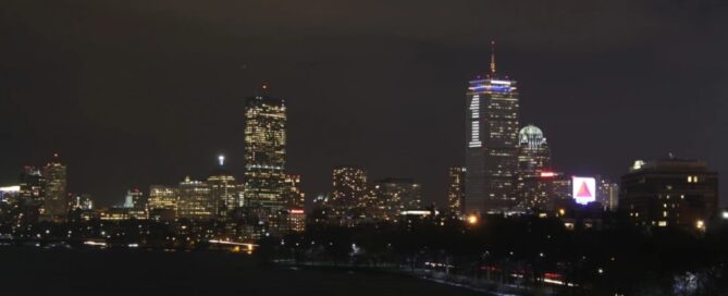The nighttime city skyline of Boston, with illuminated skyscrapers overlooking a dark waterfront under a cloudy sky, stands as a beacon of resilience, much like the essential services provided by the local rape crisis center.