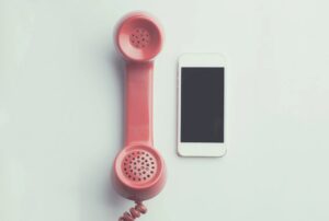 Un teléfono de disco rojo se encuentra junto a un teléfono inteligente blanco sobre una superficie clara.