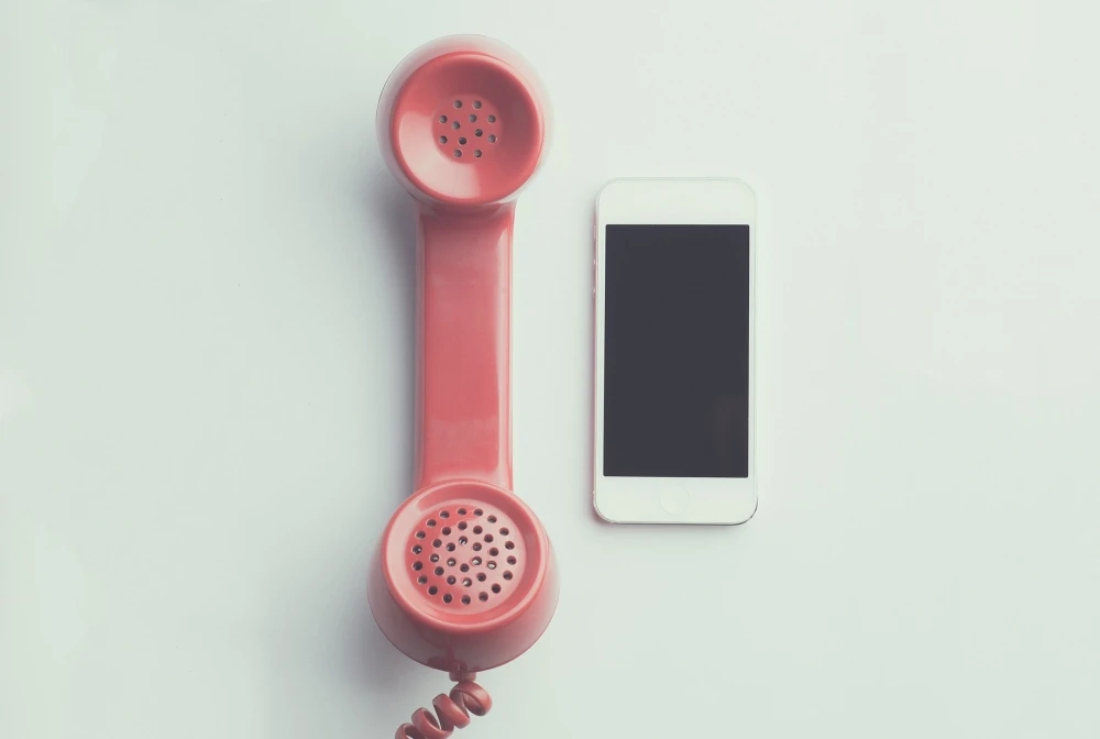 A pink vintage telephone handset is placed next to a modern smartphone on a white surface, symbolizing the bridge between past and present as we continue to advance services like those offered by the rape crisis center.