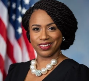 A person with braided hair and a pearl necklace stands in front of an American flag, smiling, as they recount their inspiring journey working with Boston's vital rape crisis center services.