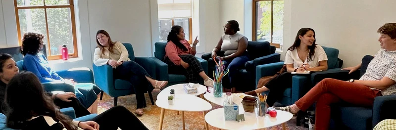 A group of people is sitting and passionately conversing in a room with blue armchairs and small round tables, united by a shared mission.