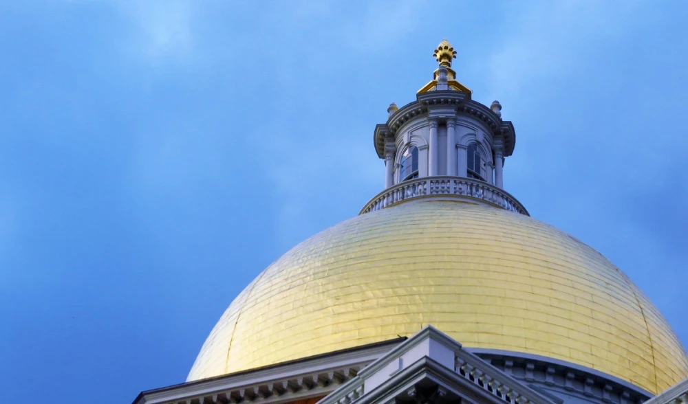 StateHouse_1000_588 A close-up of a gold-domed building with ornate architectural details stands majestically against a clear blue sky, symbolizing the ever-changing laws and rich history woven into its grand architecture.