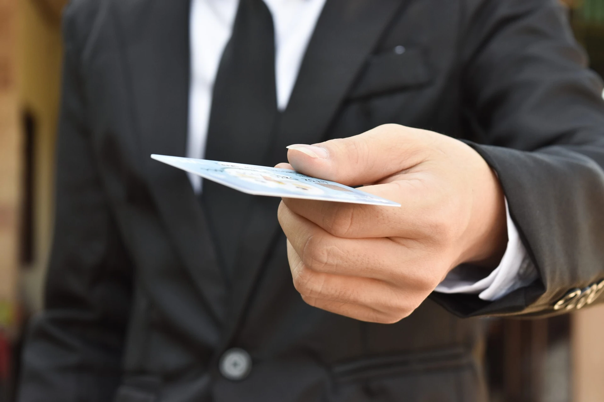 Close-up of a person in a suit demonstrating one of the many ways to give by gracefully handing over a card.