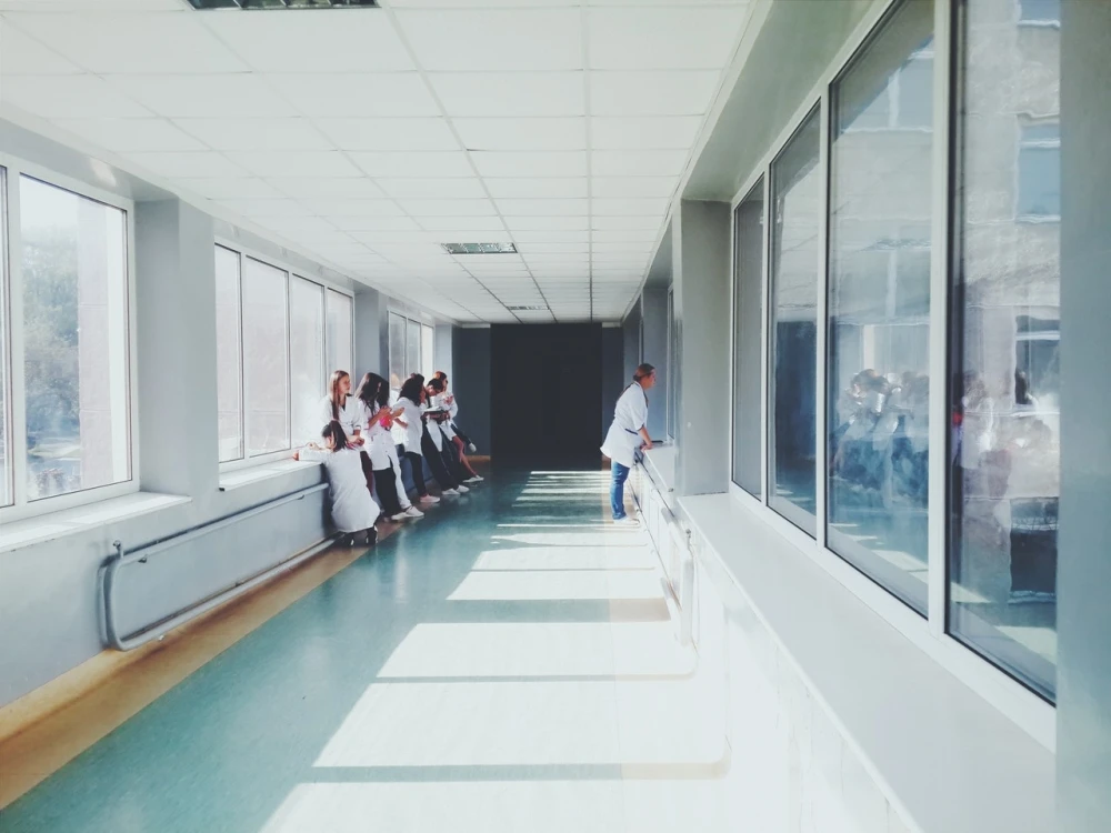 A group of people in white coats stand in a brightly lit hospital corridor, with one person looking thoughtfully out the window, reflecting on the essential services provided by the Boston hospital's rape crisis center.