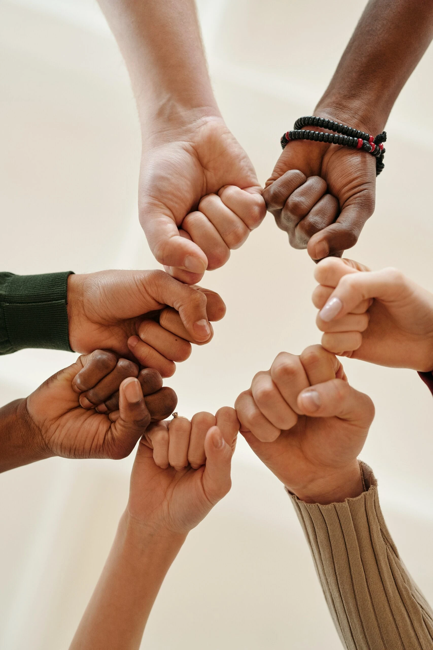 A circle of diverse hands forms a unity gesture with fists touching in the center, symbolizing strength and collective support to get help.