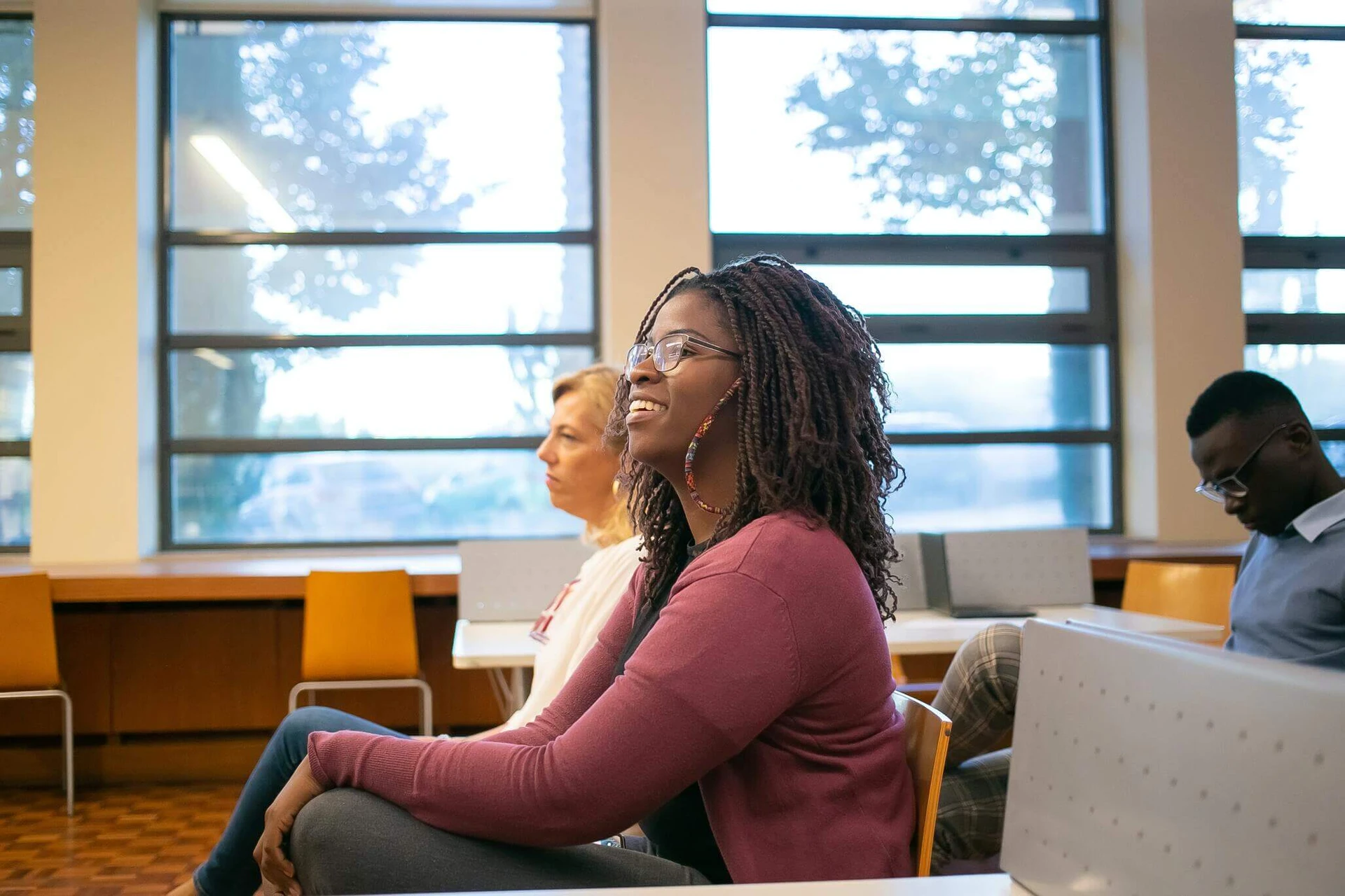 pexels-kampus-production-5940830 In a sunlit room with large windows, two women sit in the foreground while a man checks his phone, possibly looking for services to get help in Boston.