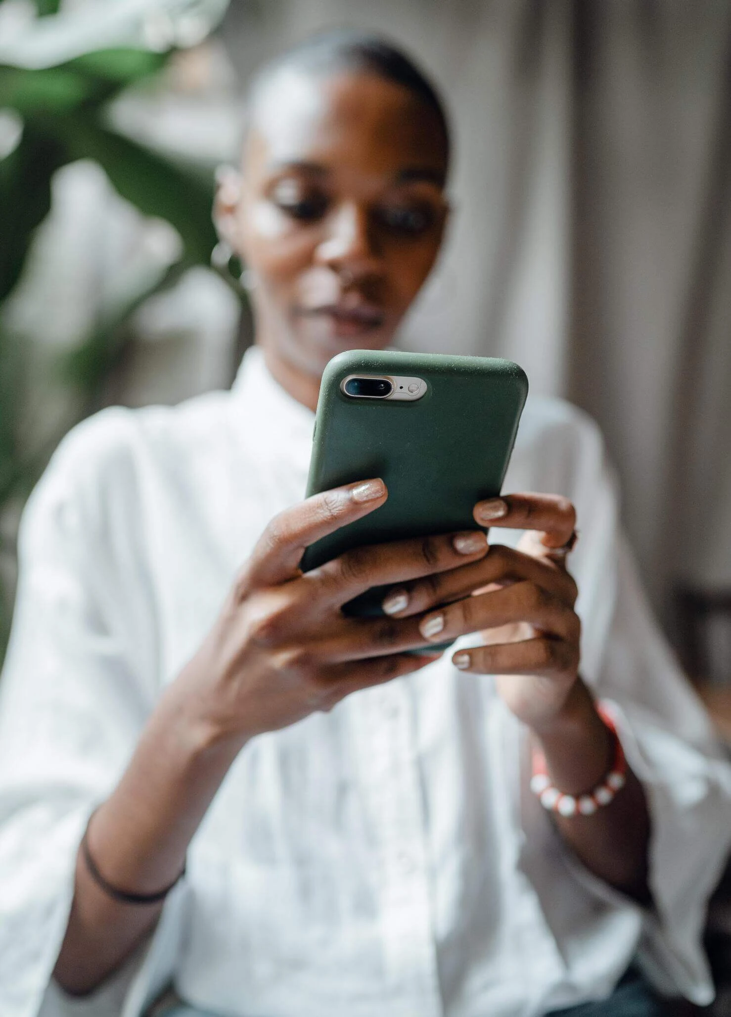 A person in a white shirt looks at a smartphone with a green case, perhaps searching for services or ways to get help in Boston.
