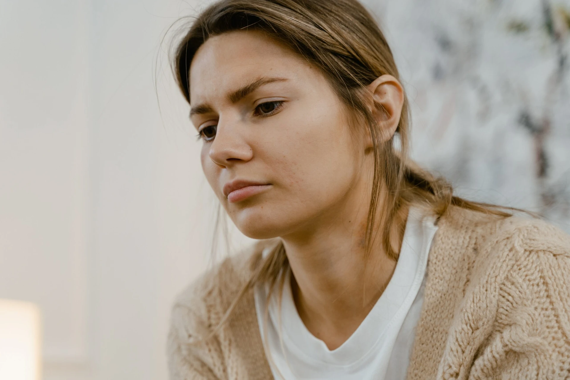 A woman with long hair, wearing a light sweater and white shirt, seems deep in thought as she considers how to get help.