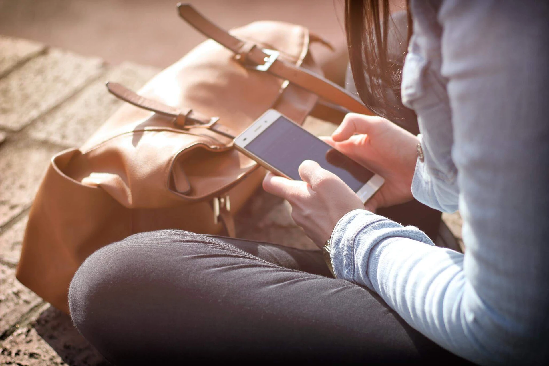 A person sits on steps in Boston, using a smartphone while a brown bag rests nearby. Perhaps they're reaching out to get help from a local support network or even connecting with resources at the rape crisis center.