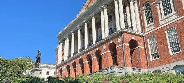 A historic red brick building with a gold dome and tall white columns houses vital services. On the lawn, a statue stands under the clear blue sky, symbolizing hope for those seeking to get help at this essential rape crisis center.