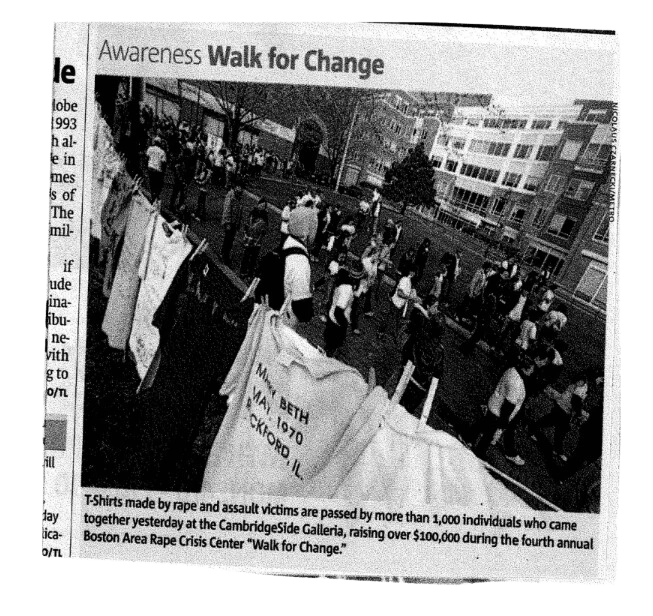 A group of people, including representatives from BARCC, are participating in the "Walk for Change" event in an urban setting, proudly wearing T-shirts and displaying signs on a fence.