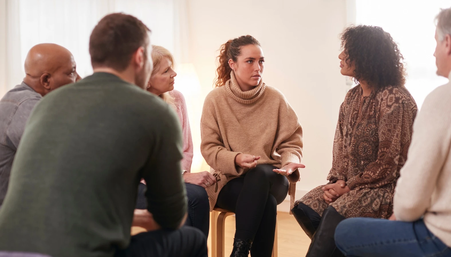 A group of people seated in a circle having a discussion about frequently asked questions in a bright room.