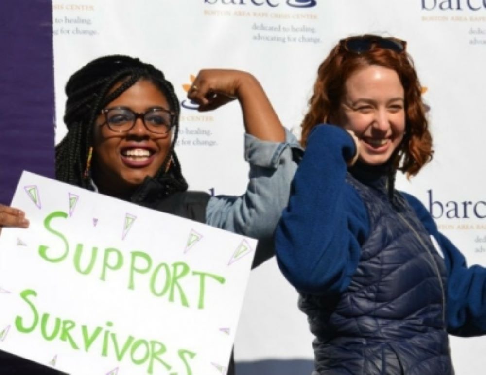 Two people smiling and flexing their arms; one holds a sign that reads "Support Survivors." It's time to take action and stand strong together.