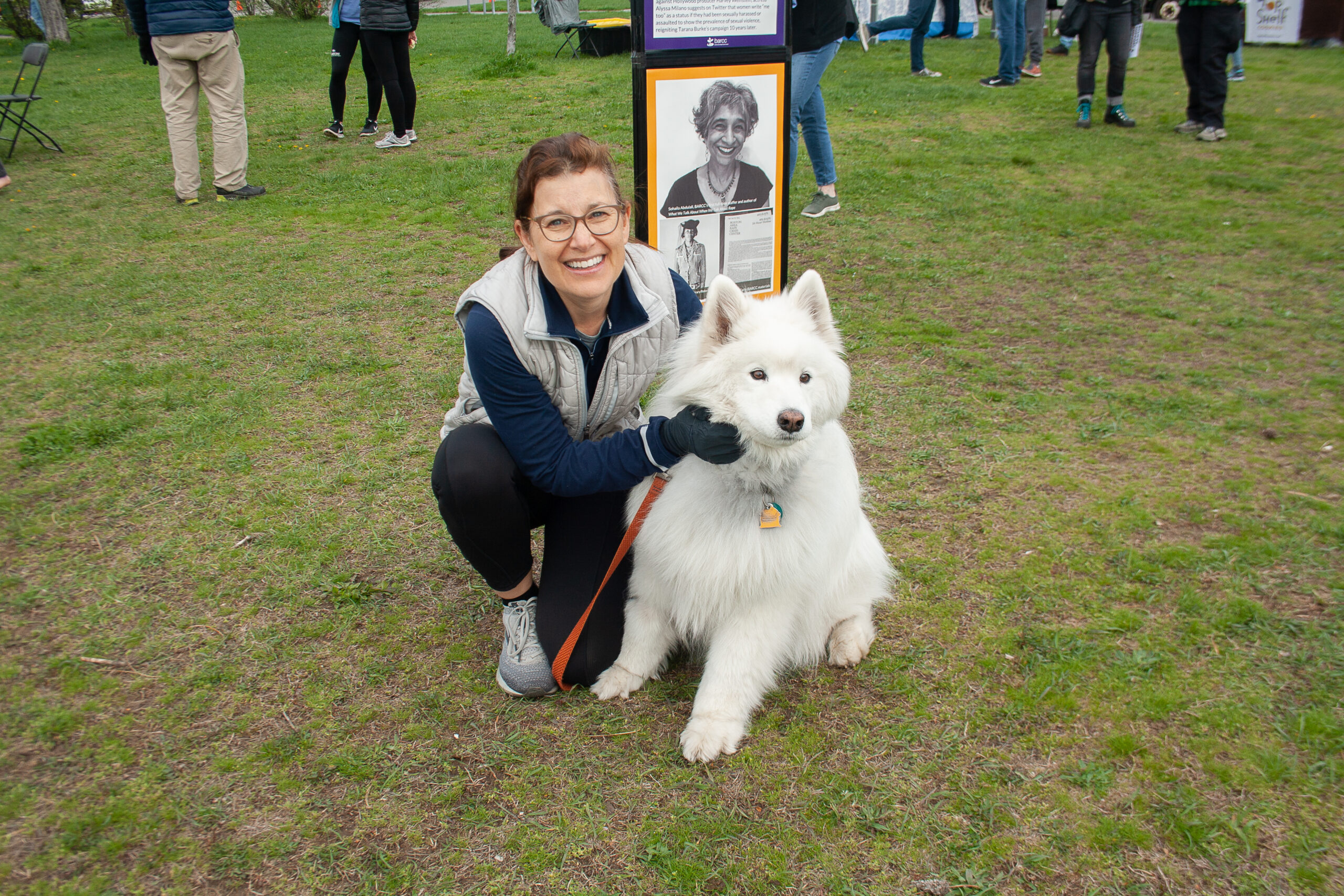 A person crouches beside a fluffy white dog on the grass, both gazing at the camera. Behind them, a sign with a black-and-white photo adds an air of mystery, hinting at facts and myths waiting to be unraveled.