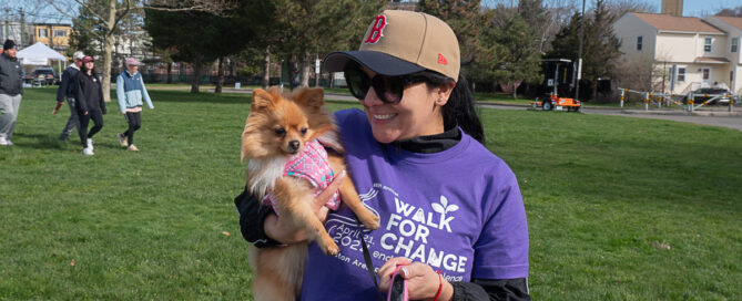 A person in a purple "Walk for Change" shirt holds a small dog that they brought to BARCC's 2024 Walk for Change fundraising event.