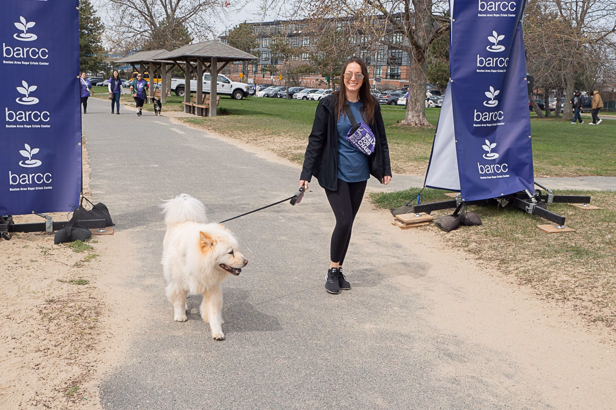 A woman walks a fluffy white dog on a leash along a path, surrounded by barcc banners that challenge myths with empowering facts.