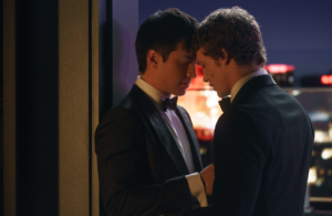 Two men in tuxedos stand close together, heads touching and eyes closed, in an intimate moment against a city nightscape—capturing the romance and artistry often seen in Liz Speakman’s evocative photography.