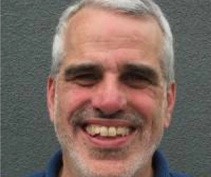 Smiling man with short, gray hair and beard in front of a gray background.