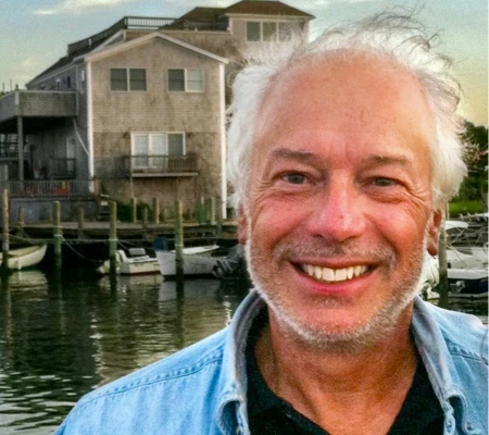 Edward Reiss, the BARCC Treasurer smiling a the camera in front of a house on a river