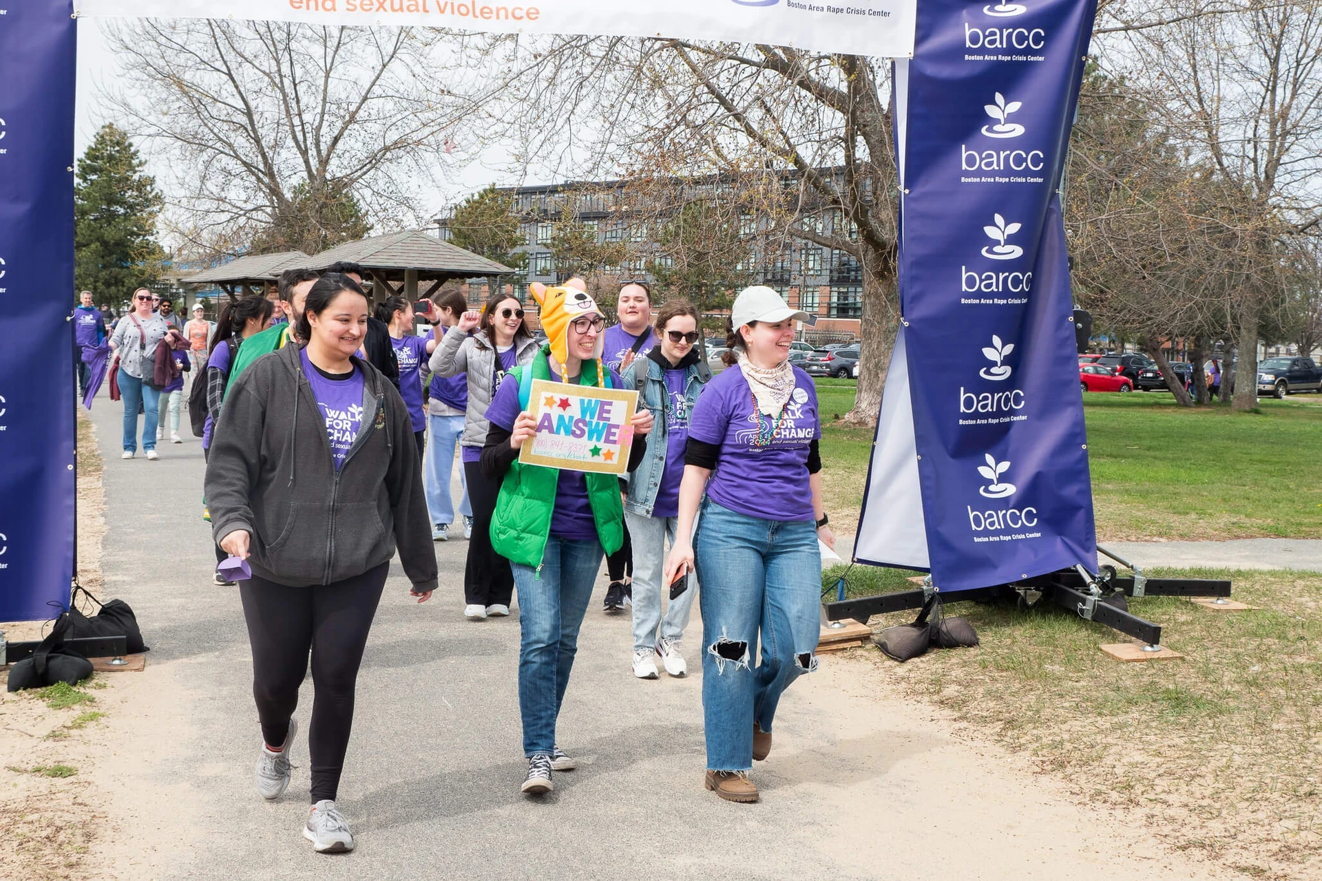 A group of people walk under a banner at an outdoor event focused on the education and prevention of sexual violence, with one person proudly holding a sign that says "We Can Soar.