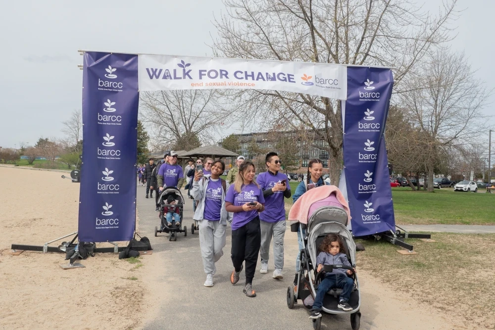 Group of people wearing green and purple "Walk for Change" shirts, standing on a wet path in front of houses, smiling and posing for a photo.
