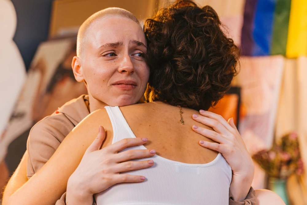 Two people embracing, one with a shaved head appearing emotional, in a vibrantly decorated room. It's a touching scene reminiscent of the supportive services you might find in Boston where people get help when they need it most.