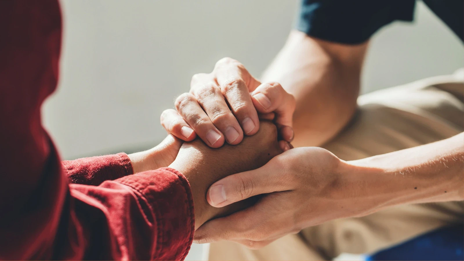 Dos personas tomadas de la mano en un gesto de apoyo, con un par de manos agarrando suavemente a la otra.