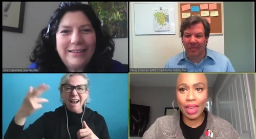 A virtual meeting with four people unfolds. The top two individuals are smiling, while the bottom left person gestures animatedly. The bottom right person, donning a pin on their jacket representing support services, is passionately speaking about ways to get help through a local initiative.