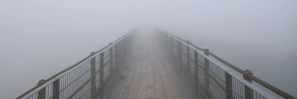 Amidst a foggy Boston morning, the narrow wooden and metal bridge stretches out, disappearing into the mist, much like seeking solace from the distant railings of support.