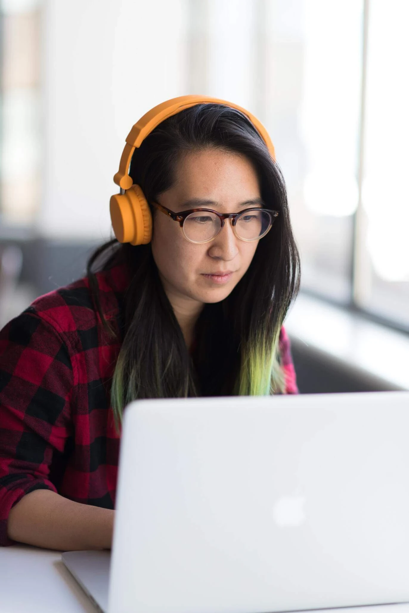 A person wearing orange headphones and glasses is deeply focused on their laptop, exploring services to get help from a nearby support center.