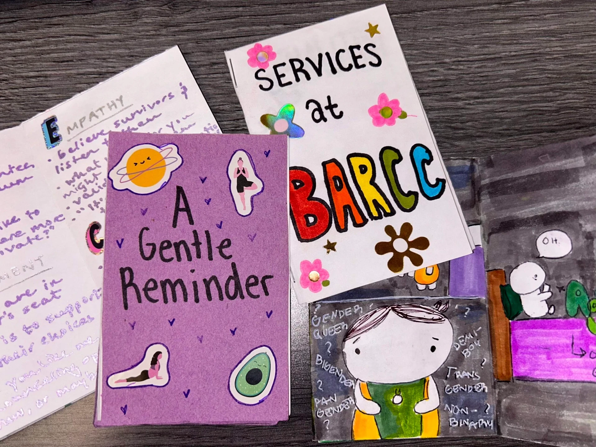 A set of colorful hand-drawn pamphlets on a table, including titles like "A Gentle Reminder" and "Services at BARCC," featuring decorative illustrations and doodles, alongside vibrant pieces introducing the Youth Leadership Corps.