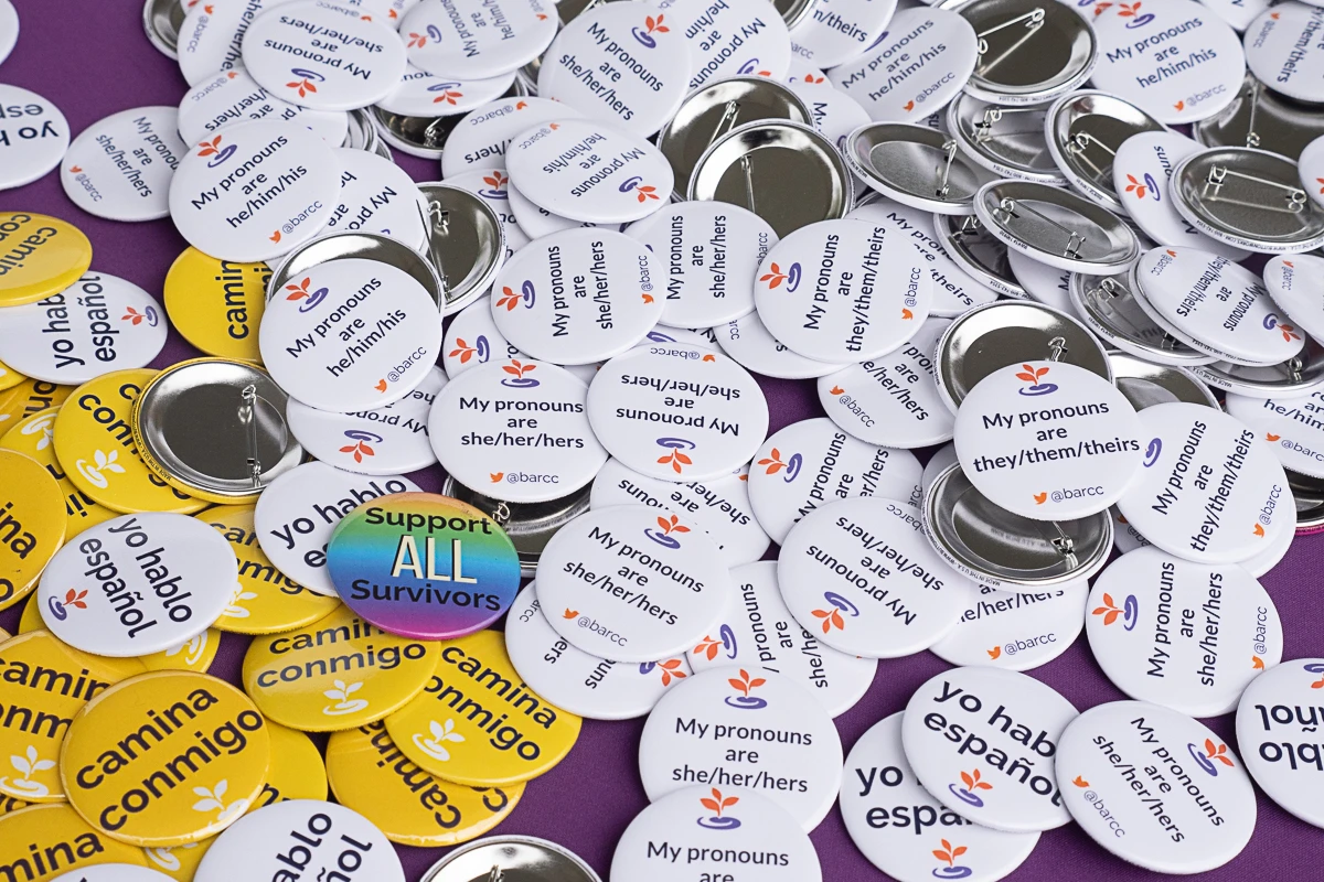 A pile of round buttons, including ones labeled with English and Spanish pronoun statements and others with phrases in Spanish, displayed on a purple surface.