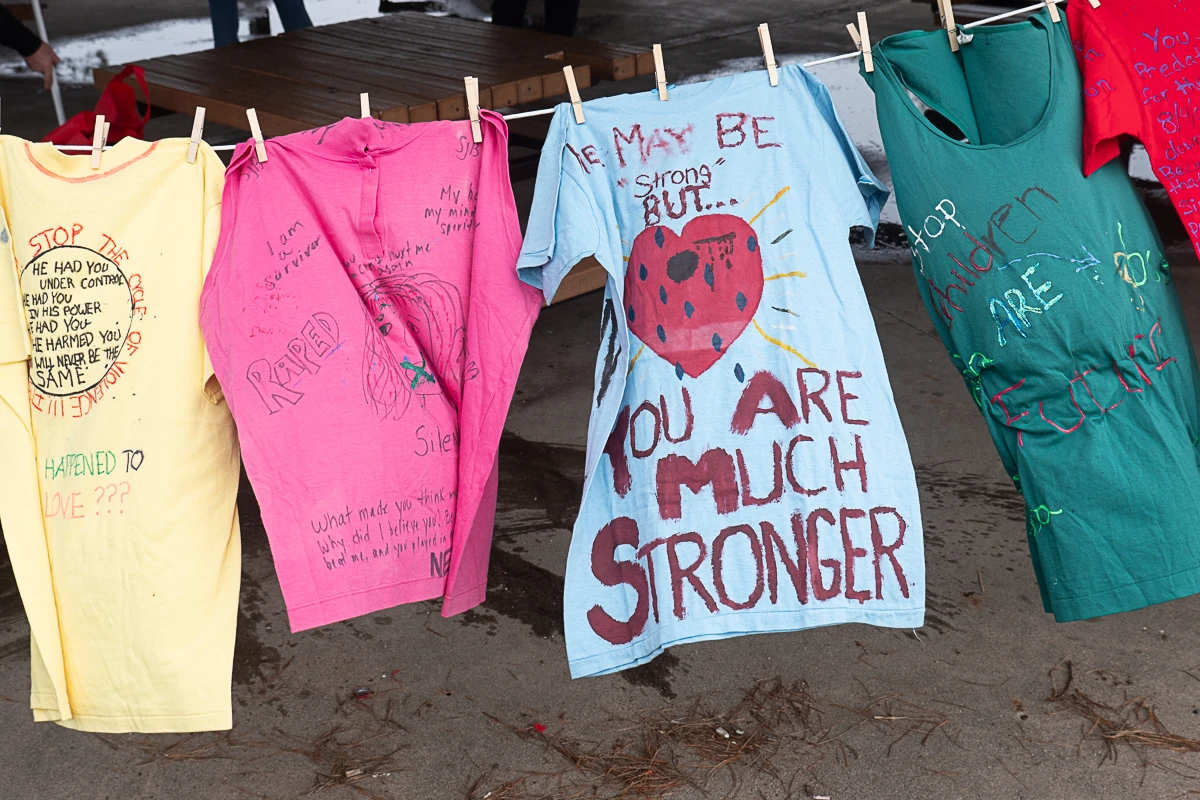Colorful t-shirts with handwritten messages about strength and resilience hang on a clothesline, part of an awareness display addressing personal and social challenges.