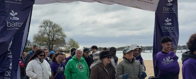 A group of people, including survivors, walk under a "Walk for Change: end sexual violence" banner on a sandy path during an organized SAAM event.